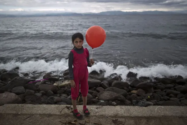 In this photo taken on Friday, October 2, 2015, Syrian refugee Raghad Faleh, 8, who came with her family from Idlib, Syria, poses for a picture while holding a balloon given to her by volunteers, a few hours after she and her family arrived on a dinghy from the Turkish coast to the northeastern Greek island of Lesbos. "My feet are killing me from pain, I walked a lot", Faleh said. (Photo by Muhammed Muheisen/AP Photo)