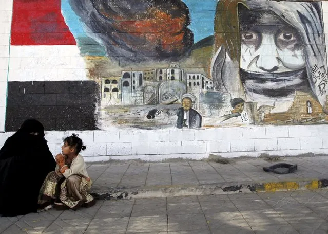 A woman and a girl sit next a graffiti painted by pro-Houthi activists on the gate of the Saudi embassy in Yemen's capital Sanaa October 21, 2015. (Photo by Khaled Abdullah/Reuters)