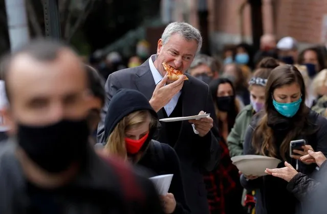New York City Mayor Bill de Blasio eats pizza as he stands in line with hundreds of other voters for several hours to cast his ballot during early voting in the Brooklyn borough of New York City, New York, U.S., October 27, 2020. (Photo by Mike Segar/Reuters)
