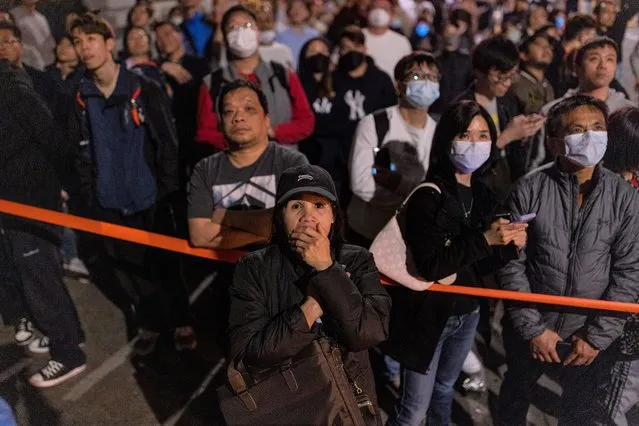 Residents and others look on as a fire burns at a construction site in Hong Kong, Friday, March 3, 2023. The fire erupted at the site of The Mariners’ Club redevelopment project in the densely populated Tsim Sha Tsui district at about 11 p.m. on Thursday night. (Photo by Louise Delmotte/AP Photo)