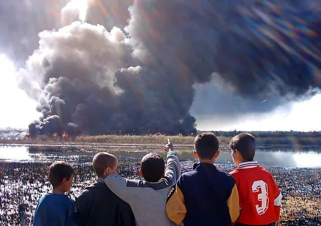 A group of Iraqi boys gather to watch smoke billowing from burning oil on the outskirts of the town of Baiji, north of Baghdad, March 15, 2005. (Photo by Sabah Hamid/Reuters)