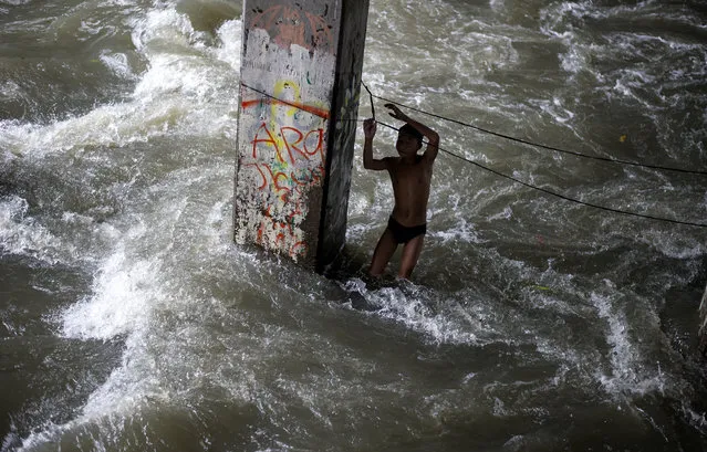 A boy plays in a swollen creek under a bridge in Manila on October 16, 2016. Typhoon Sarika lashed the main Philippine island of Luzon on October 16, flattening homes and toppling trees and power pylons as more than 12,000 people fled to safer ground, officials said. Shanties built beside a river, under a creek are the usual victims of floodings. (Photo by Noel Celis/AFP Photo)