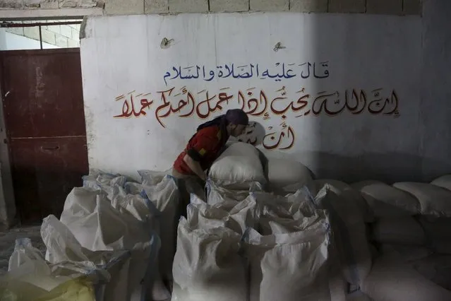 A worker arranges bags of flour inside a bakery in the rebel-controlled area of Maaret al-Numan town in Idlib province, Syria December 17, 2015. The text on the wall reads in Arabic: “He said, peace be upon him, that god loves if one of you worked a job to do it well”. (Photo by Khalil Ashawi/Reuters)