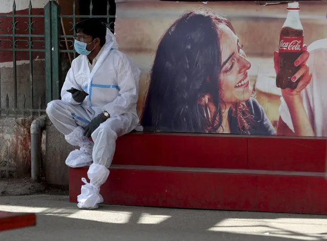 A health worker wearing personal protective equipment takes a break as he awaits travelers to arrive outside a a train station in Bengaluru, India, Monday, February 22, 2021. Cases of COVID-19 are increasing in some parts of India after months of a steady nationwide decline, prompting authorities to impose lockdowns and other virus restrictions. (Photo by Aijaz Rahi/AP Photo)