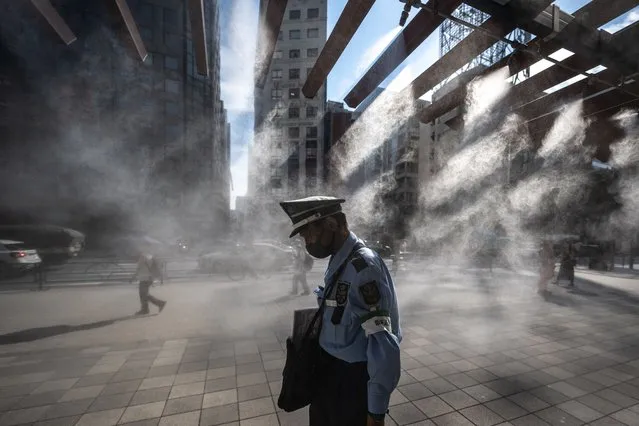 A security guard walks past an overhead water misting system on a hot day in the Ginza district of Tokyo on July 10, 2023. (Photo by Philip Fong/AFP Photo)