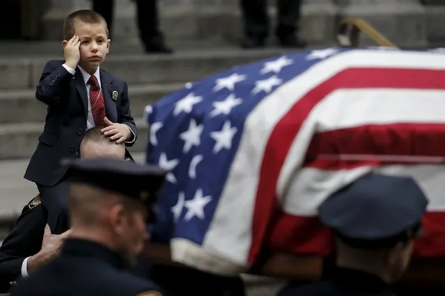 Ryan Lemm, 4, salutes as he is carried by New York Police Department officer John McCrossen as he watches the casket of his father, NYPD officer Joseph Lemm, who was killed on duty in Afghanistan, following funeral services in the Manhattan borough of New York, December 30, 2015. McCrossen was Lemm's partner in the NYPD Warrant Squad. Lemm was one of six U.S. troops killed by a suicide bomber near Bagram air base in Afghanistan. (Photo by Carlo Allegri/Reuters)