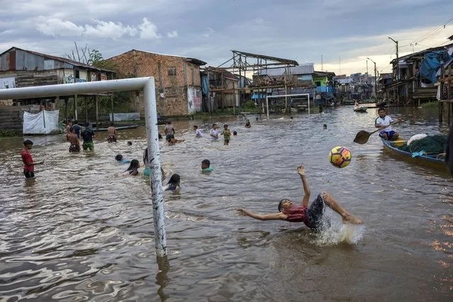 A boy bicycle kicks a ball in a flooded area of the Belen community in Iquitos, Peru, Saturday, March 20, 2021. (Photo by Rodrigo Abd/AP Photo)