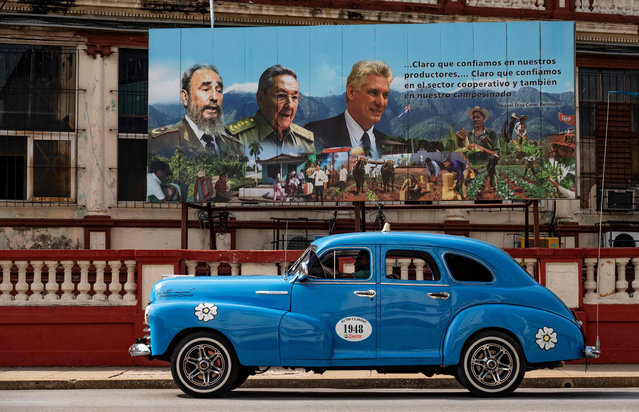 An old American car passes near a poster of Cuban late leader Fidel Castro (L), Former President Raul Castro (C) and current President Miguel Diaz-Canel (R) in Havana, on August 17, 2023. (Photo by Yamil Lage/AFP Photo)