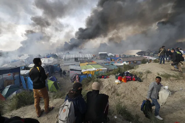 Smoke rises the sky as migrants and journalists look at burning makeshift shelters and tents in the “Jungle” on the third day of their evacuation and transfer to reception centers in France, as part of the dismantlement of the camp in Calais, France, October 26, 2016. (Photo by Philippe Wojazer/Reuters)
