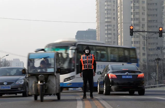 Artist Liu Bolin wearing a vest with 24 mobile phones stands in the middle of a road during morning rush hour as he live broadcasts air pollution in the city on the fourth day after a red alert was issued for heavy air pollution in Beijing, China, December 19, 2016. (Photo by Jason Lee/Reuters)