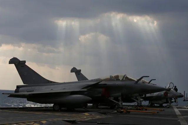 The sun breaks through clouds above Rafale (L) and a Super Etendards fighter jets seen aboard France's Charles de Gaulle aircraft carrier in the Gulf, January 29, 2016. (Photo by Philippe Wojazer/Reuters)