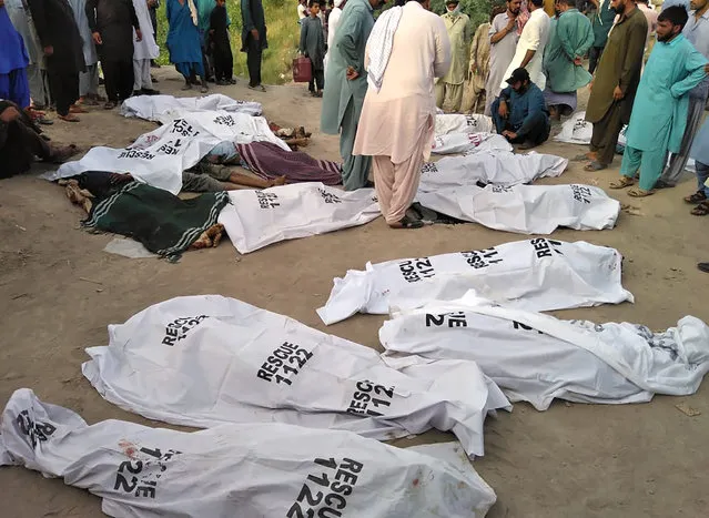 In this handout photo released by Punjab Province's Emergency Service Rescue 11222, shows people gathering around covered bodies close to the site of a deadly bus accident near Dera Ghazi Khan, Pakistan, Monday, July 19, 2021. (Photo by Emergency Service Rescue 1122 via AP Photo)