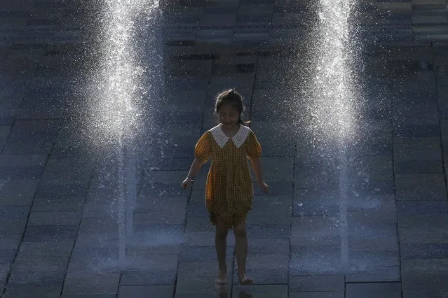 A young girl runs through a fountain in Beijing, China, Thursday, August 26, 2021. (Photo by Ng Han Guan/AP Photo)
