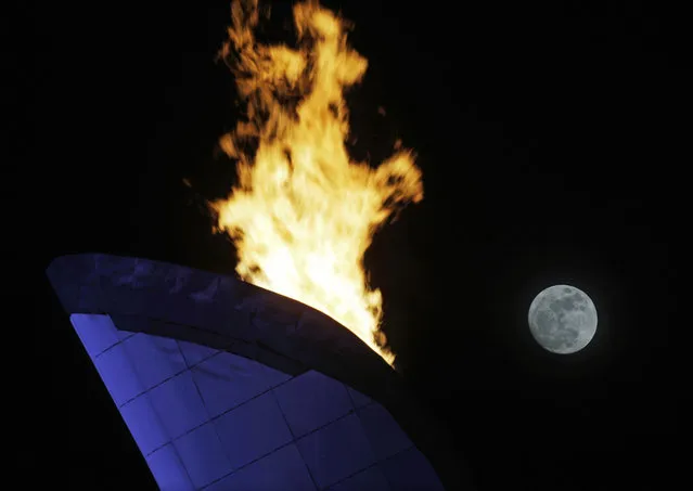 The moon is seen rising past the flame from the Olympic cauldron at the 2014 Winter Olympics, Thursday, Feb. 13, 2014, in Sochi, Russia. (Photo by Morry Gash/AP Photo)