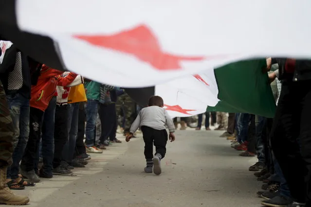 A boy walks under an opposition flag during an anti-government protest in the rebel-controlled area of Maaret al-Numan town in Idlib province, Syria March 25, 2016. (Photo by Khalil Ashawi/Reuters)