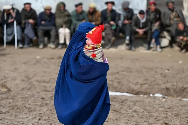 An Afghan burqa-clad woman carries a child as she walks along a street in Argo district of Badakhshan province on February 25, 2024. (Photo by Wakil Kohsar/AFP Photo)