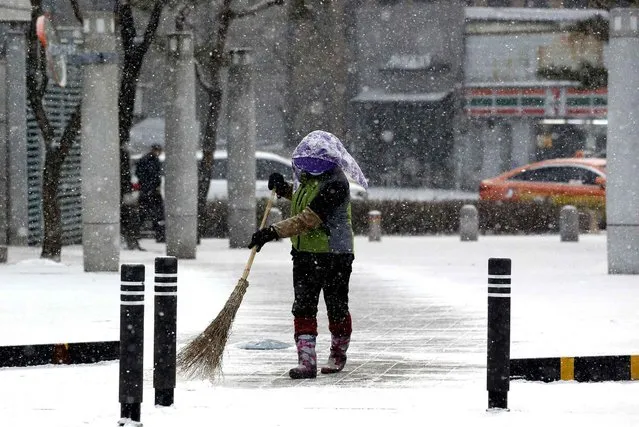 A woman sweeps snow off with a broom in Seoul, South Korea, Tuesday, January 26, 2016. The temperatures dropped to –8 degrees Celsius (17.6 degrees Fahrenheit) in the morning. (Photo by Lee Jin-man/AP Photo)