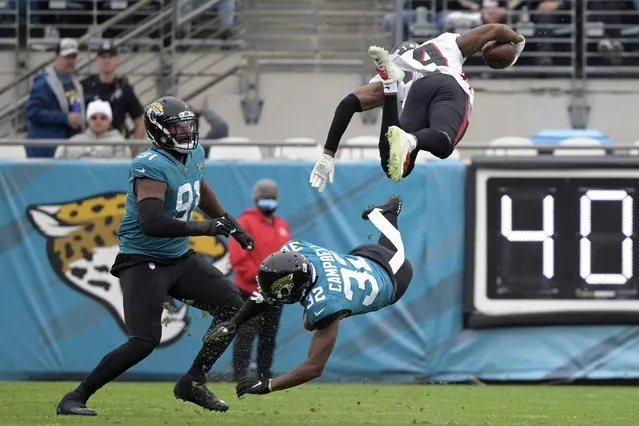 Atlanta Falcons wide receiver Russell Gage, top right, leaps over Jacksonville Jaguars cornerback Tyson Campbell (32) and defensive end Dawuane Smoot, left, after a reception during the first half of an NFL football game, Sunday, November 28, 2021, in Jacksonville, Fla. (Photo by Phelan M. Ebenhack/AP Photo)
