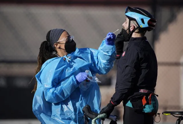 A medical technician performs a nasal swab test on a cyclist queued up in a line with motorists at a COVID-19 testing site near All City Stadium Thursday, December 30, 2021, in southeast Denver. With the rapid spread of the omicron variant paired with the Christmas holiday, testing sites have been strained to meet demand both in Colorado as well as across the country. (Photo by David Zalubowski/AP Photo)