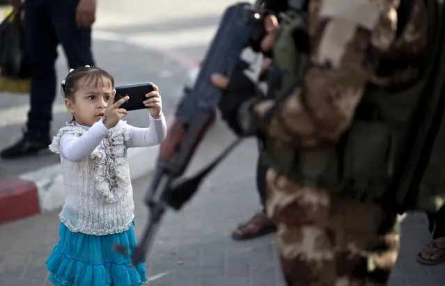 A young girl takes a photo of a member of the Ezzedine al-Qassam Brigades, the military wing of the Palestinian Islamist movement Hamas, during a rally marking Palestinian Prisoner Day in Gaza City on April 16, 2016. (Photo by Mahmud Hams/AFP Photo)