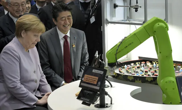 German Chancellor Angela Merkel, left, and the Prime Minister of Japan, Shinzo Abe, right, attend the presentation of a robot serving sushi during a walkabout at the IT trade fair CeBIT in Hanover, Germany, Monday, March 20, 2017. (Photo by Jens Meyer/AP Photo)