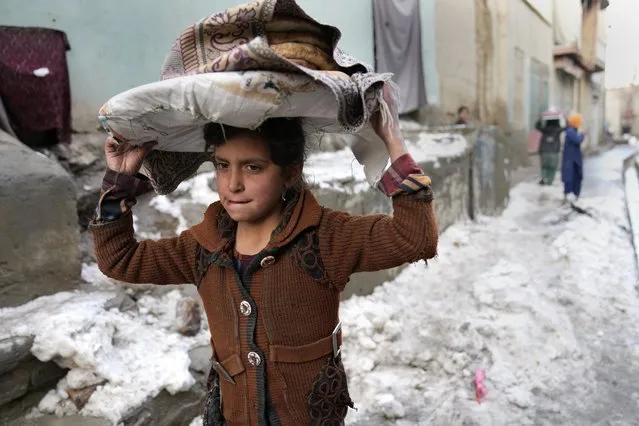 A girl carries breads on her head as she walks in the snow, in Kabul, Afghanistan, Tuesday, February 8, 2022. (Photo by Hussein Malla/AP Photo)