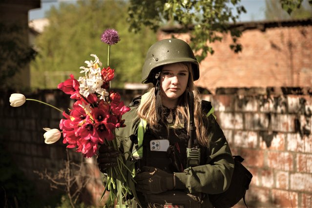 A girl named Milanka poses for a photo after collecting flowers near damaged building amid Russia-Ukraine war in frontline city of Huliaipole, South Ukraine on May 12, 2023. A group of volunteers helps on the construction of the first invincibility point in the city. (Photo by Andre Alves/Anadolu Agency via Getty Images)