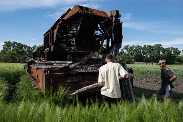 Men scavenge burnt Russian military vehicle for parts and scrap metal is seen in the field on June 4, 2022 in Novyi Bykiv, Ukraine. Chernihiv, northeast of Kyiv, was an early target of Russia's offensive after its Feb. 24 invasion. While they failed to capture the city, Russian forces battered large parts of Chernihiv and the surrounding region in their attempted advance toward the capital. (Photo by Alexey Furman/Getty Images)