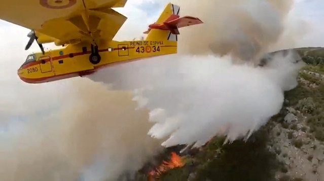 A firefighting plane dumps water on burning vegetation during a wildfire, in the Canary Islands, Spain in this screengrab taken from a handout video released on August 17, 2023. (Photo by Canary Islands Territory Ministry via Reuters)