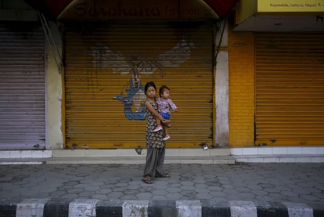 A girl carrying a child stands in front of closed shops as she watches protesters (unseen) march on the road during the general strike organised by a 30-party alliance led by a hardline faction of former Maoist rebels, who are protesting against the draft of the new constitution, in Lalitpur, Nepal August 16, 2015. (Photo by Navesh Chitrakar/Reuters)