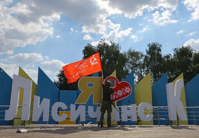 A service member of pro-Russian troops holds a Soviet-era flag, which was raised to mark the anniversary of the victory over Nazi Germany in World War Two, at a monument “I love Lysychansk” during Ukraine-Russia conflict in the city of Lysychansk in the Luhansk Region, Ukraine on July 4, 2022. (Photo by Alexander Ermochenko/Reuters)