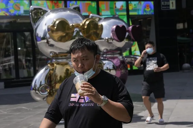 A man lowers his mask to drink from a cup as he past near a mall, Wednesday, July 13, 2022, in Beijing. (Photo by Ng Han Guan/AP Photo)