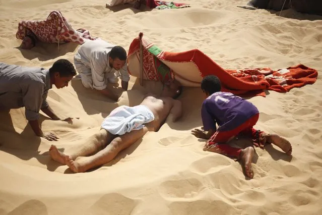 Workers help to bury a patient in the sand during his sand bath in Siwa, Egypt, August 12, 2015. (Photo by Asmaa Waguih/Reuters)