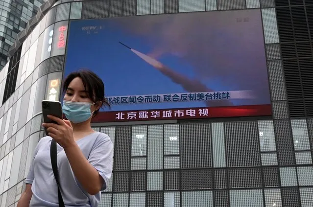 A woman uses her mobile phone as she walks in front of a large screen showing a news broadcast about China's military exercises encircling Taiwan, in Beijing on August 4, 2022. China's largest-ever military exercises encircling Taiwan kicked off August 4, in a show of force straddling vital international shipping lanes after a visit to the island by US House Speaker Nancy Pelosi. (Photo by Noel Celis/AFP Photo)