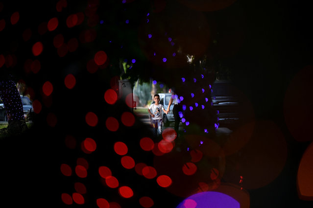 A boy walks by trees decorated with Christmas lights, as the Christmas season kicks off as per a decree of Venezuela's President Nicolas Maduro, in Caracas, Venezuela on October 1, 2024. (Photo by Gaby Oraa/Reuters)