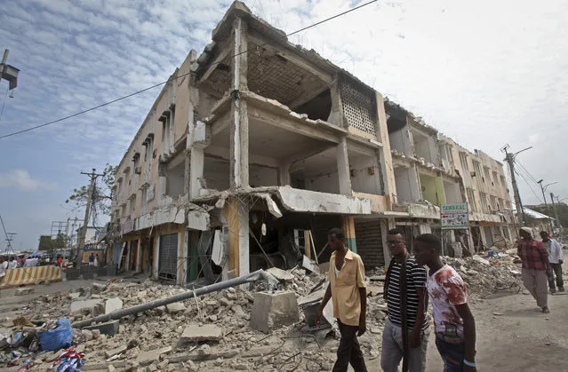 Men walk near destroyed buildings as thousands of Somalis gathered to pray at the site of the country's deadliest attack and to mourn the hundreds of victims, at the site of the attack in Mogadishu, Somalia Friday, October 20, 2017. More than 300 people were killed and nearly 400 wounded in Saturday's truck bombing, with scores missing. (Photo by Farah Abdi Warsameh/AP Photo)