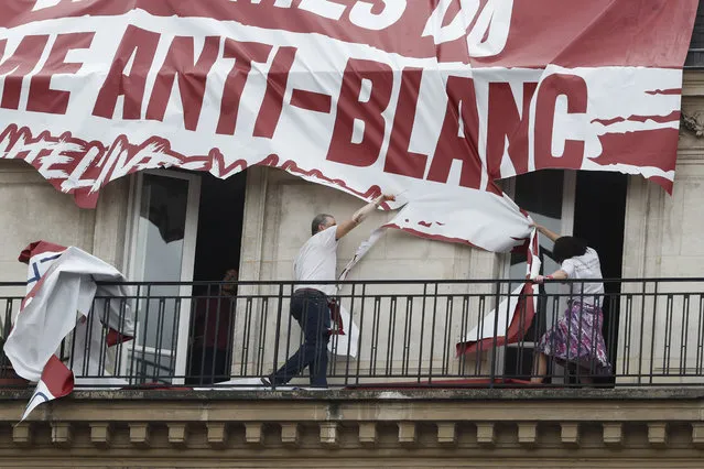 Residents of a building cut up a banner which was lowered from the roof of his building by far-right protestors with the Identitarian nationalist French movement during a march against police brutality and racism in Paris, France, Saturday, June 13, 2020, organized by supporters of Adama Traore, who died in police custody in 2016 in circumstances that remain unclear despite four years of back-and-forth autopsies. The march is expected to be the biggest of several demonstrations Saturday inspired by the Black Lives Matter movement in the U.S., and French police ordered the closure of freshly reopened restaurants and shops along the route fearing possible violence. (Photo by Thibault Camus/AP Photo)