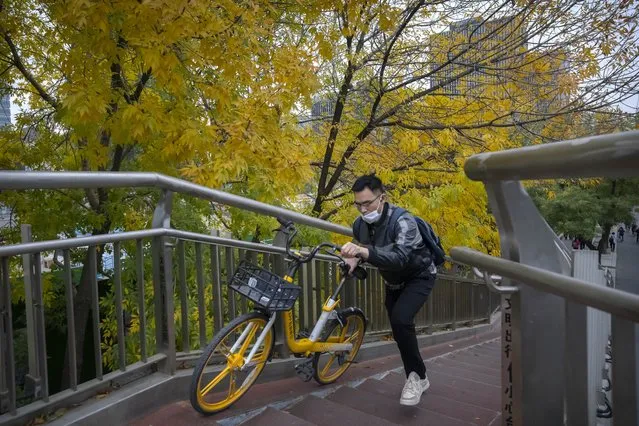 A commuter wearing a face mask pushes a bicycle across a pedestrian bridge in the central business district in Beijing, Friday, October 28, 2022. (Photo by Mark Schiefelbein/AP Photo)