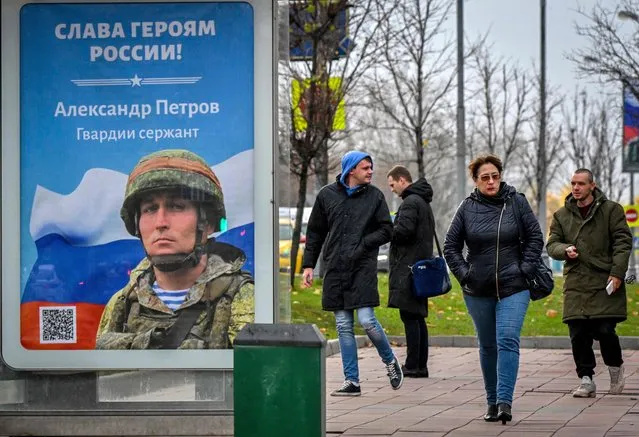 Pedestrians walk past a poster displaying a Russian soldier with a slogan reading “Glory to the Heroes of Russia” decorating a bus stop in Moscow on October 24, 2022. (Photo by Yuri Kadobnov/AFP Photo)