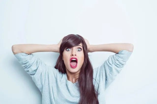 Portrait of shocked young woman wearing grey jumper, raising her arms and shouting at camera, rolling eyes. Studio shot, white background. (Photo by Izusek/Getty Images)