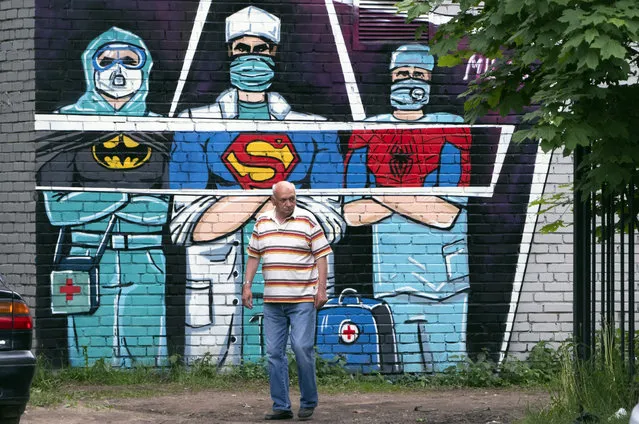 A man walks past a graffiti depicting medical workers struggling with coronavirus as superheroes in Vsevolozhsk, outside St.Petersburg, Russia, Monday, June 15, 2020. (Photo by Dmitri Lovetsky/AP Photo)