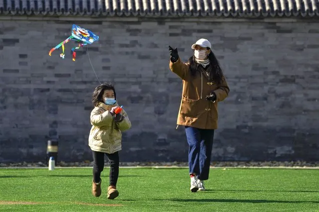 A woman and a child fly kite on a green outside a mall in Beijing, Sunday, December 4, 2022. (Photo by Andy Wong/AP Photo)
