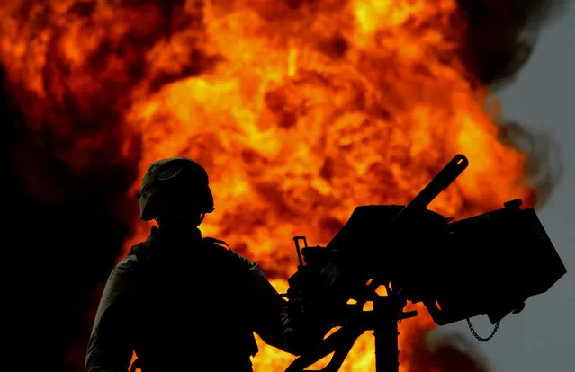 A U.S. Army soldier atop a Humvee armed with a heavy machine gun secures an area by a burning oil well in Iraq's vast southern Rumaila oilfields, on March 30, 2003. U.S. engineers moved through the oilfields on Sunday shutting down wellheads in an operation that could take months to complete. (Photo by Yannis Behrakis/Reuters/The Atlantic)