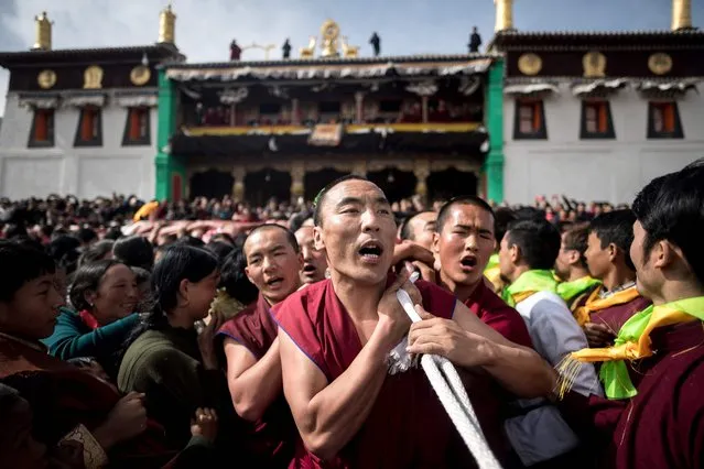 This picture taken on March 1, 2018 shows Tibetan Buddhist monks carrying a giant thangka for the unveiling ceremony during Monlam, otherwise known as the Great Prayer Festival of Losar, the Tibetan New Year, at the Rongwo Monastery, in Tongren County, Huangnan Tibetan Autonomous Prefecture, on the Qinghai-Tibet plateau. (Photo by Johannes Eisele/AFP Photo)