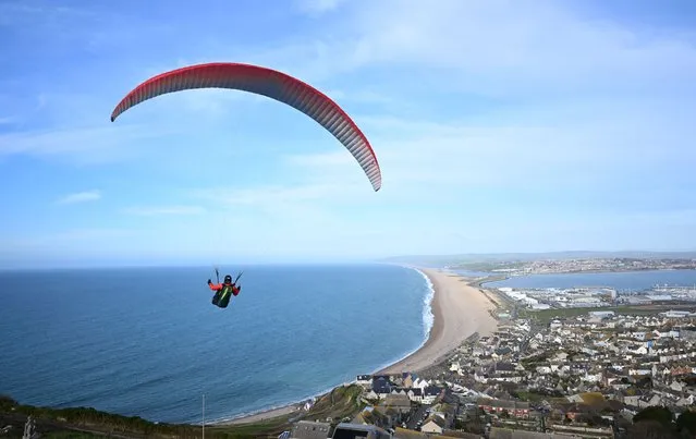 A paraglider enjoys the weather as they fly over Chesil beach in Dorset, on February 19, 2023 in Portland, England. (Photo by Finnbarr Webster/Getty Images)