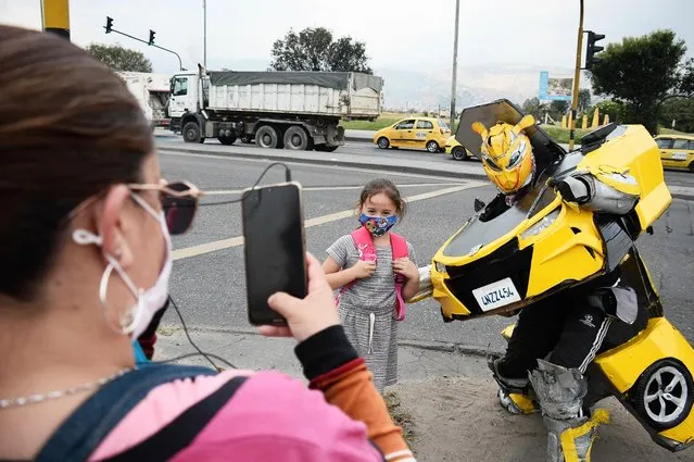 A woman takes a photo of her daughter with Luis Cruz while working in his transformers suit at a traffic light in Bogota, Colombia on January 26, 2022. The story of Luis Cruz, a man who decided to create to scale the robots from the movie Transformers, which marked his childhood and because of his family's situation he was never able to obtain a toy of his characters. More than ten years ago he used these costumes created by him in a specific traffic light, in which he can make 20 transformations (from car to robot) in one hour, together with his family they have created different robots and Luis has managed to be recognized in different spaces and exhibitions for his work. (Photo by Lina Gasca M/Anadolu Agency via Getty Images)