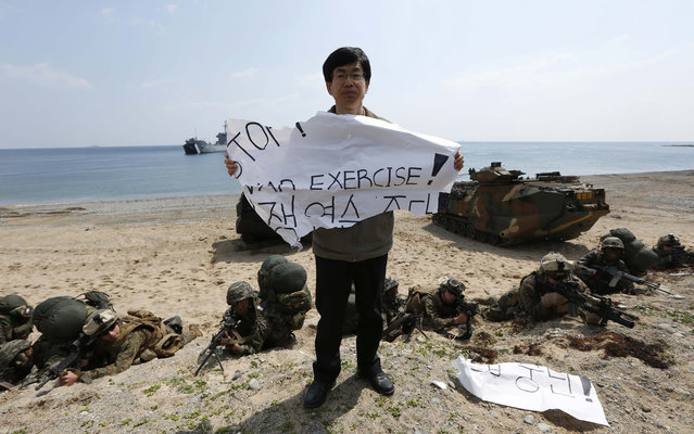 An anti-war protester holding a banner reading “Stop War Exercise” in front of the U.S. Marines and their South Korean counterparts during the joint military exercises between South Korea and the United States called Ssangyong 2013 as a part of annual Foal Eagle military exercises in Pohang, south of Seoul, South Korea, Friday, April 26, 2013. (Photo by Kin Cheung/AP Photo)