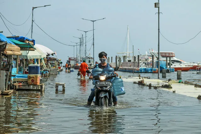 Residents are seen walking through tidal floods that hit at Muara Angke area in North Jakarta, Indonesia on November 19, 2020. (Photo by Nofiq Hidayat/Riau Images/Barcroft Media via Getty Images)