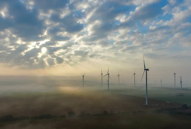 A picture taken with a drone shows the morning sun behind clouds over the mist enveloped landscape on a wind energy park near Sieversdorf in the district of Oder-Spree, Brandenburg, Germany, 10 September 2016. (Photo by Patrick Pleul/EPA)