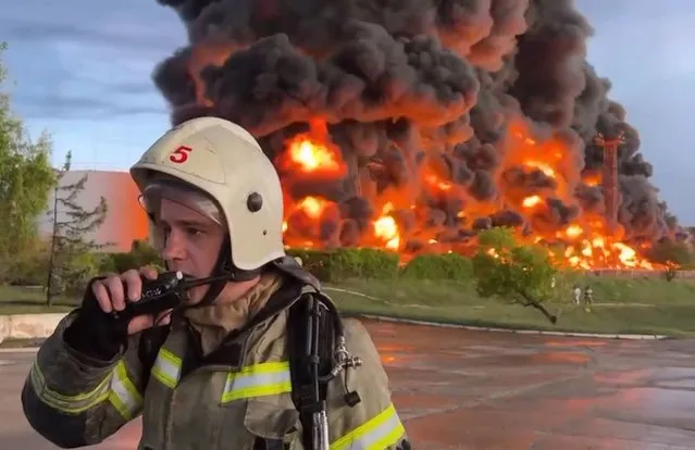 In this handout photo made from video released by the Governor of Sevastopol Mikhail Razvozhaev telegram channel on Saturday, April 29, 2023, a firefighter speaks on the walkie talkie as smoke and flame rise from a burning fuel tank in Sevastopol, Crimea. A massive fire erupted at an oil reservoir there after it was hit by a drone, a Russian-appointed official there reported on Saturday. (Photo by Sevastopol Governor Mikhail Razvozhaev telegram channel via AP Photo)